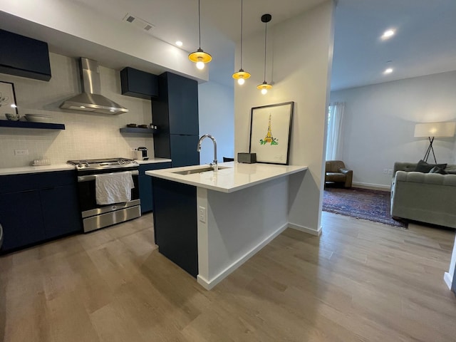 kitchen featuring wall chimney exhaust hood, visible vents, a sink, stainless steel gas range oven, and dark cabinetry