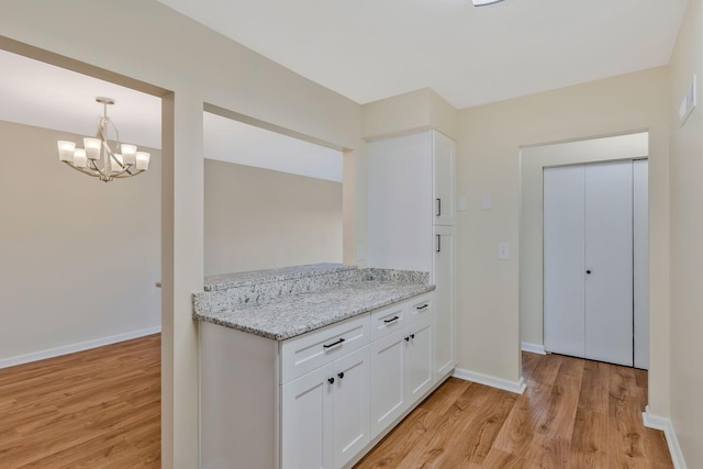 kitchen featuring light wood-style flooring, white cabinets, light stone counters, a notable chandelier, and baseboards
