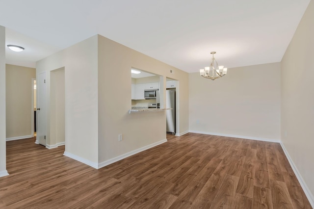 spare room with baseboards, a chandelier, and wood finished floors