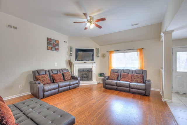 living room featuring light wood-style flooring, ceiling fan, a fireplace with raised hearth, and visible vents