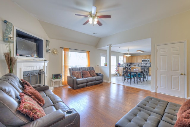 living room with a fireplace, light wood-type flooring, a ceiling fan, and lofted ceiling