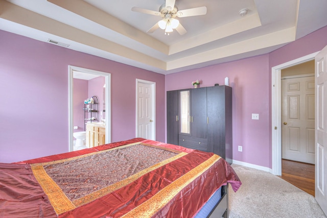 bedroom featuring baseboards, carpet flooring, ensuite bathroom, visible vents, and a tray ceiling