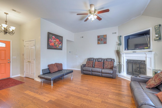 living area featuring a brick fireplace, visible vents, ceiling fan with notable chandelier, and wood finished floors