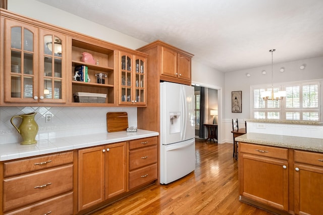 kitchen featuring white fridge with ice dispenser, light countertops, light wood-style floors, brown cabinets, and decorative backsplash
