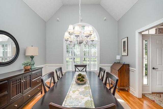 dining space with a decorative wall, a chandelier, light wood-style floors, wainscoting, and lofted ceiling