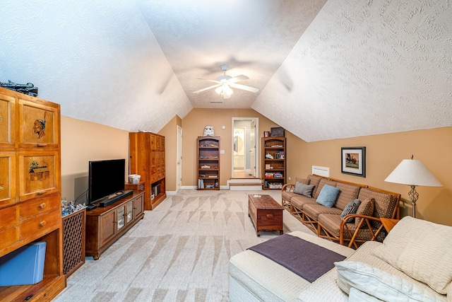 living area featuring baseboards, a ceiling fan, a textured ceiling, vaulted ceiling, and light colored carpet