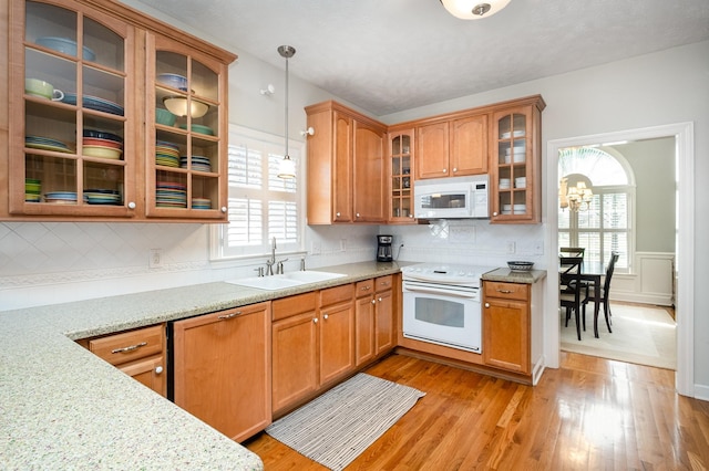 kitchen with light wood finished floors, a sink, white appliances, and glass insert cabinets