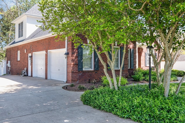 view of home's exterior with an attached garage, a shingled roof, driveway, and brick siding