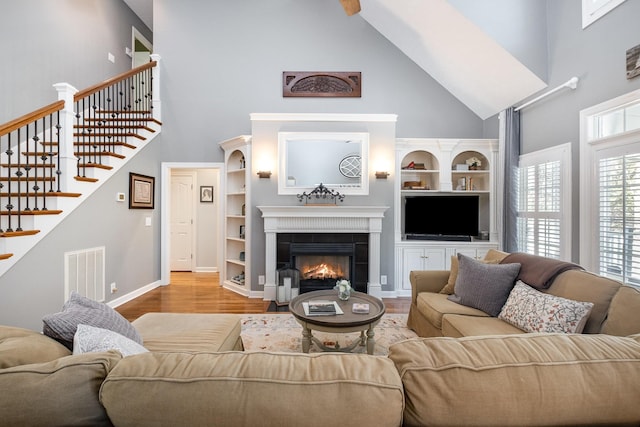 living room featuring high vaulted ceiling, a fireplace, visible vents, wood finished floors, and baseboards