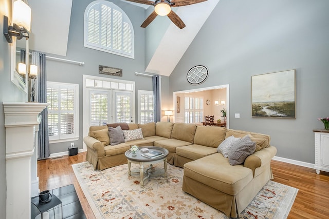 living area with ceiling fan, wood finished floors, a high ceiling, and baseboards