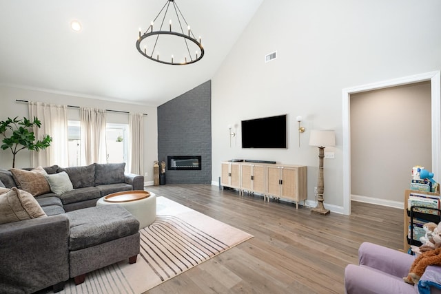living room with visible vents, a chandelier, a fireplace, wood finished floors, and high vaulted ceiling