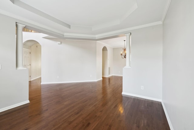 spare room with dark wood finished floors, a tray ceiling, arched walkways, ornamental molding, and baseboards