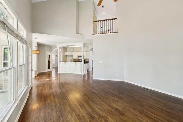unfurnished living room featuring baseboards, a ceiling fan, dark wood-type flooring, visible vents, and arched walkways