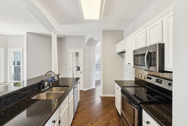 kitchen with arched walkways, dark stone countertops, appliances with stainless steel finishes, a sink, and decorative backsplash
