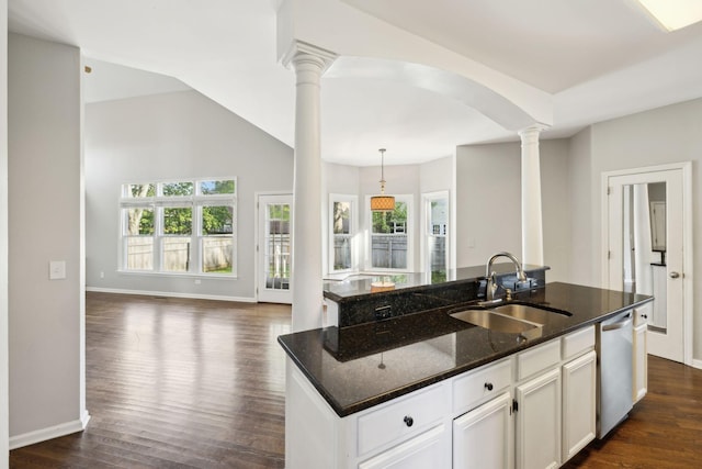kitchen featuring stainless steel dishwasher, ornate columns, a kitchen island with sink, a sink, and open floor plan