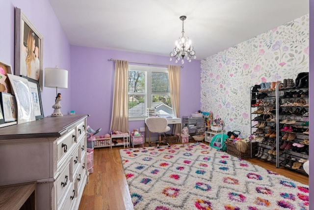 playroom featuring an accent wall, light wood-style flooring, a chandelier, and wallpapered walls