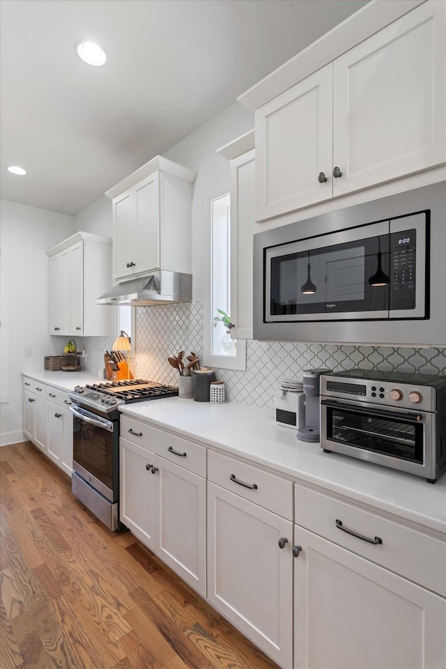 kitchen featuring appliances with stainless steel finishes, light wood finished floors, white cabinets, and under cabinet range hood