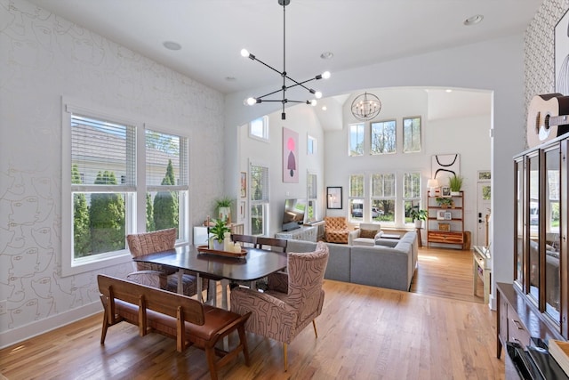 dining space featuring baseboards, a notable chandelier, light wood-type flooring, wallpapered walls, and high vaulted ceiling