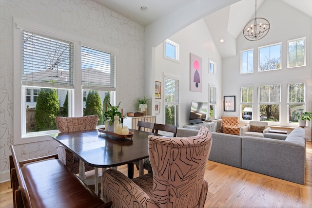 dining area featuring a chandelier, light wood-type flooring, wallpapered walls, and high vaulted ceiling