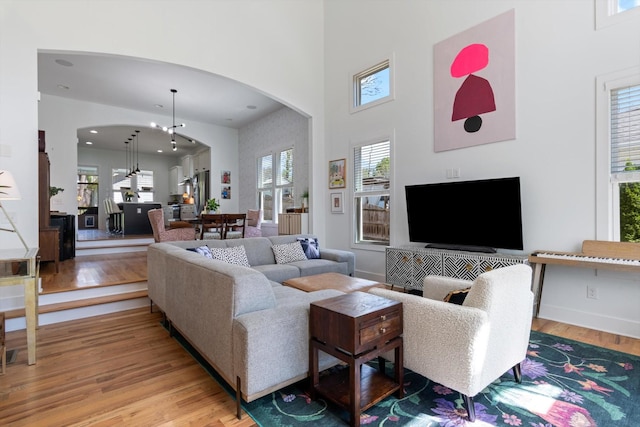 living room featuring light wood-style flooring, arched walkways, recessed lighting, a high ceiling, and baseboards