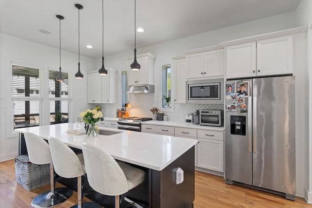 kitchen featuring a center island with sink, appliances with stainless steel finishes, light wood finished floors, and under cabinet range hood
