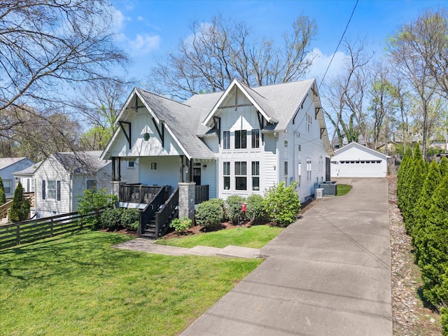 view of front of property featuring an outbuilding, a detached garage, roof with shingles, a front yard, and fence