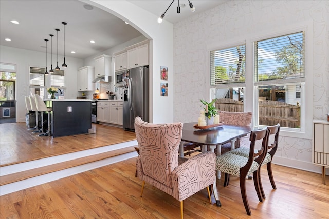 dining area featuring light wood-style floors, arched walkways, recessed lighting, wallpapered walls, and baseboards