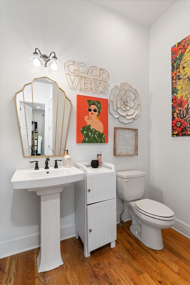 half bath featuring baseboards, toilet, and wood finished floors