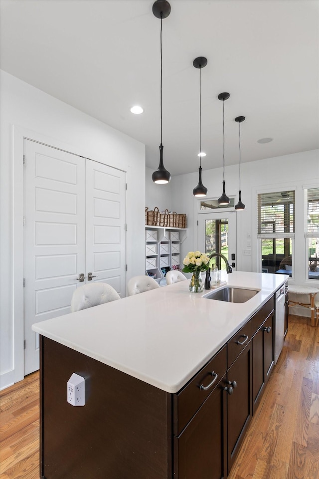 kitchen with dark brown cabinetry, open floor plan, light wood-style flooring, a kitchen island with sink, and a sink