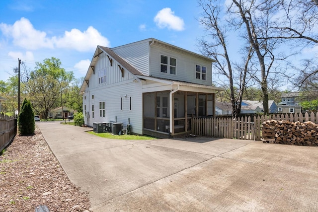 back of house featuring a sunroom, central AC unit, concrete driveway, and fence