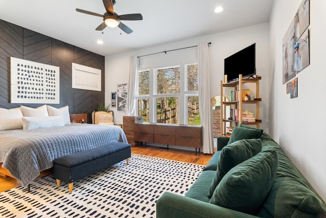 bedroom featuring recessed lighting, a ceiling fan, wood walls, an accent wall, and wood finished floors