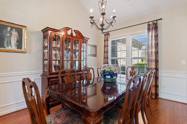 dining area featuring a chandelier, wood finished floors, wainscoting, and lofted ceiling