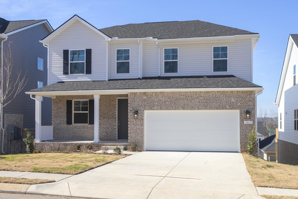 traditional home with roof with shingles, driveway, brick siding, a garage, and covered porch