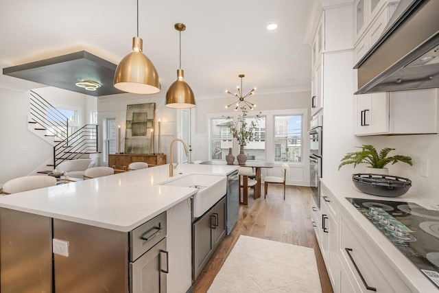 kitchen featuring light countertops, black electric stovetop, under cabinet range hood, and a sink