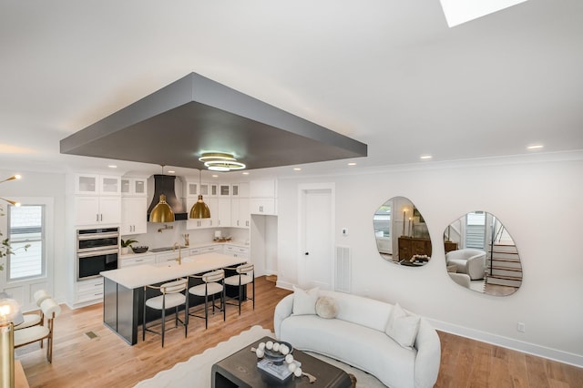 living room with visible vents, baseboards, ornamental molding, light wood finished floors, and recessed lighting