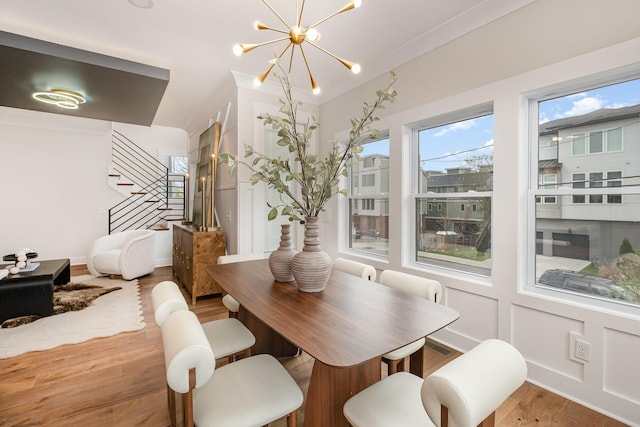 dining space featuring a decorative wall, a notable chandelier, wood finished floors, and stairs