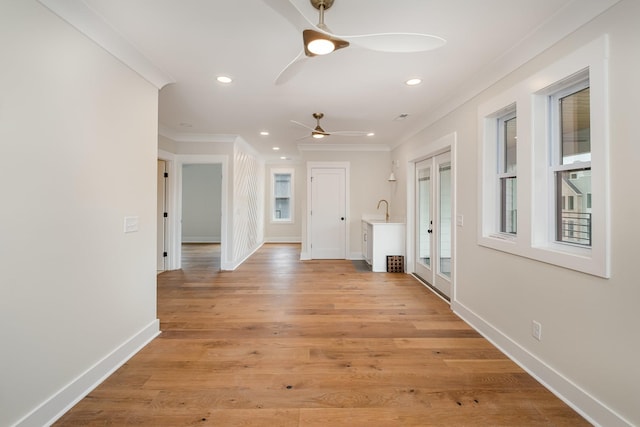 corridor featuring crown molding, a healthy amount of sunlight, baseboards, and light wood-type flooring