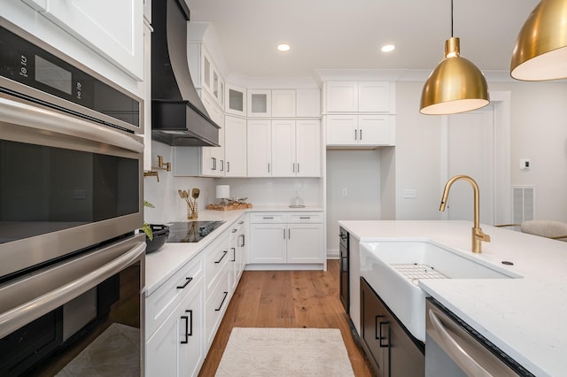 kitchen featuring white cabinets, premium range hood, a sink, and appliances with stainless steel finishes