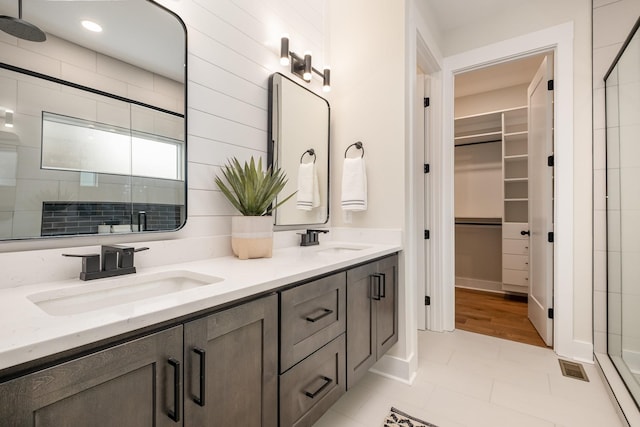 full bath with a shower stall, double vanity, a sink, and a walk in closet