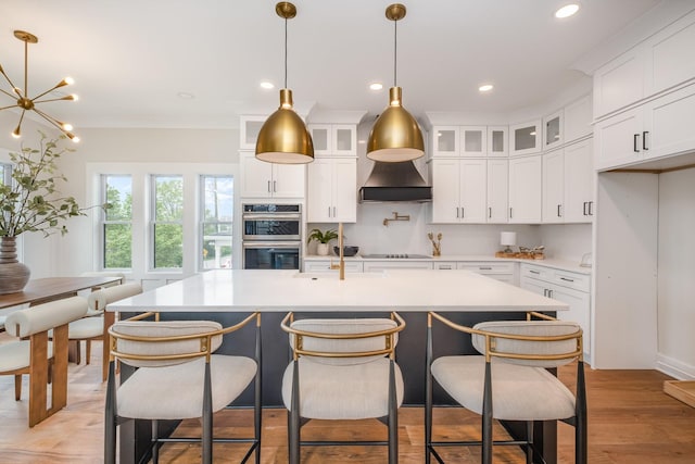 kitchen featuring black electric stovetop, wall chimney range hood, light countertops, stainless steel double oven, and light wood-style floors