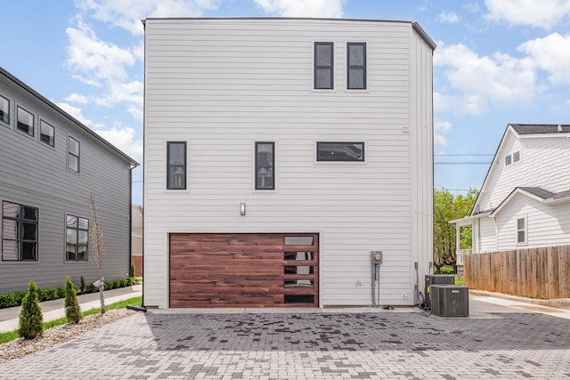 back of property with an attached garage, central air condition unit, fence, and decorative driveway