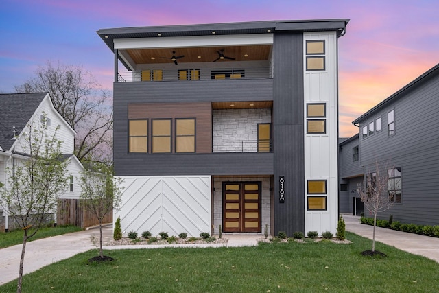 modern home with board and batten siding, ceiling fan, a lawn, and a balcony