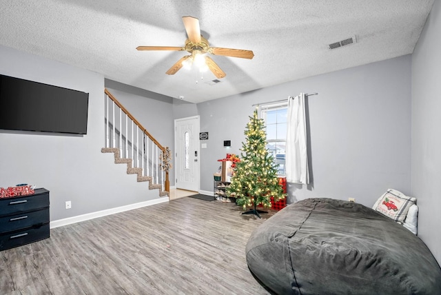 interior space featuring a ceiling fan, visible vents, stairway, wood finished floors, and baseboards