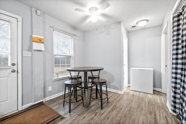 dining room featuring visible vents, baseboards, a ceiling fan, a textured ceiling, and wood finished floors