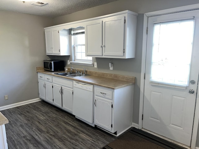 kitchen with stainless steel microwave, white cabinetry, visible vents, white dishwasher, and a sink