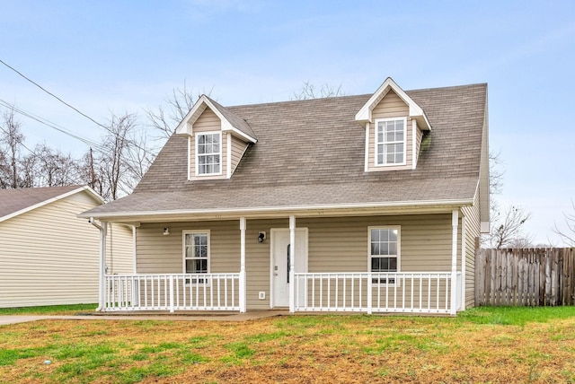 view of front of home featuring a shingled roof, a porch, fence, and a front lawn