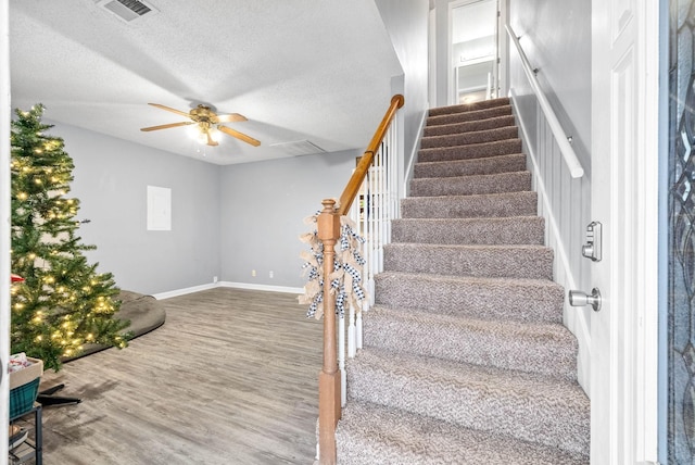 staircase featuring baseboards, a textured ceiling, visible vents, ceiling fan, and wood finished floors