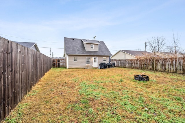 rear view of property featuring an outdoor fire pit, a fenced backyard, and a lawn