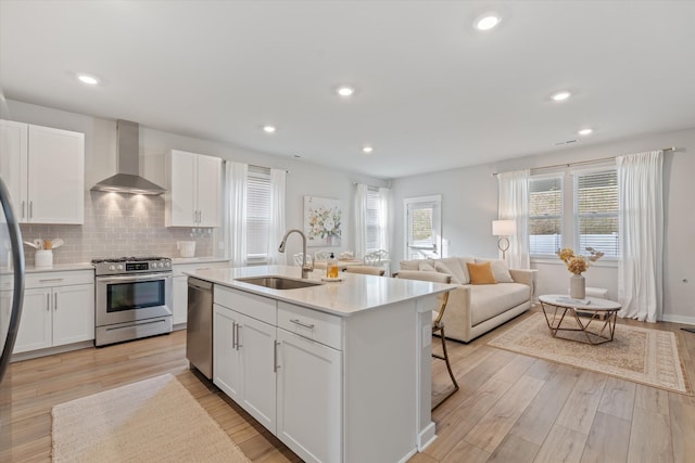 kitchen with wall chimney range hood, light countertops, stainless steel appliances, light wood finished floors, and a sink