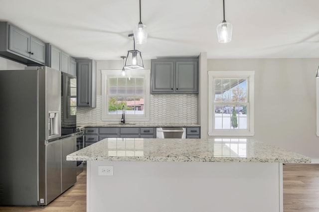 kitchen featuring gray cabinets, a sink, light wood-style floors, tasteful backsplash, and appliances with stainless steel finishes